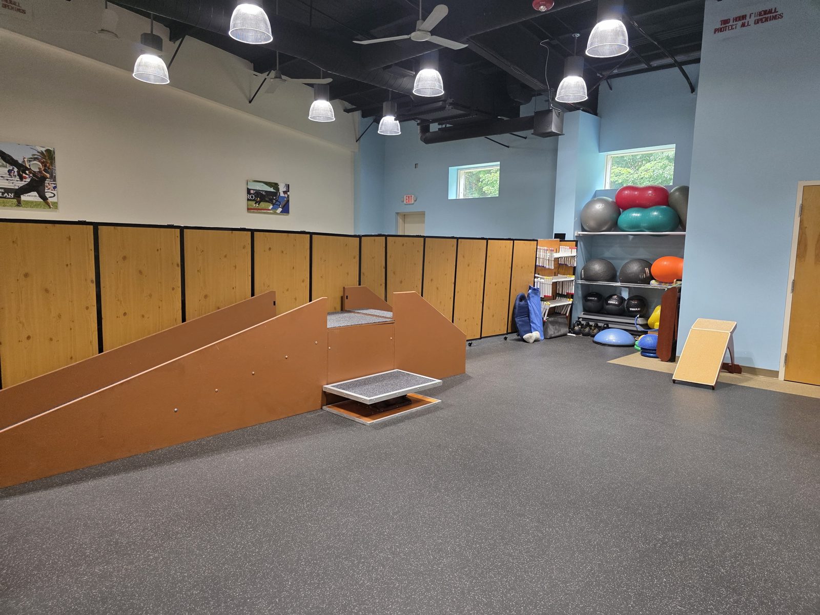 Open training floor with gait-training ramps, a raised platform, balance equipment and exercise balls